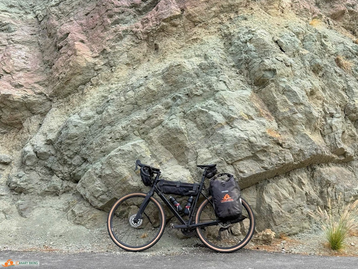 Fiets met fietstassen met Canary Biking logo tegen rotsen